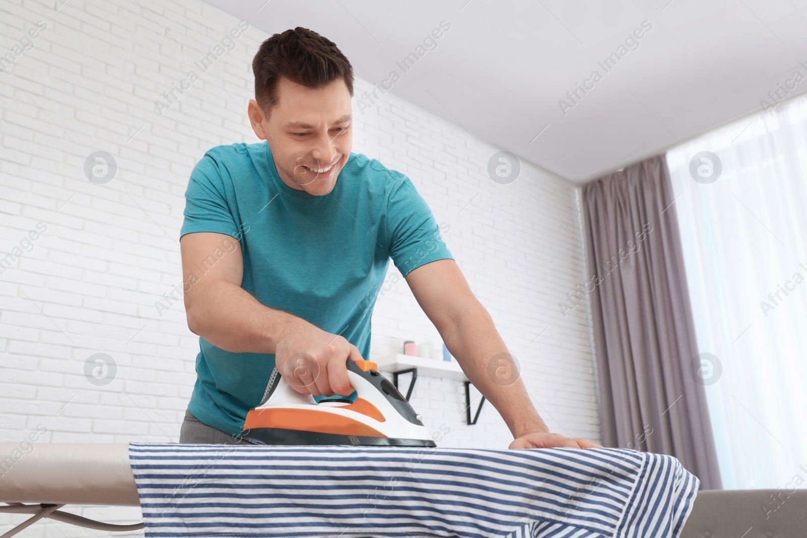 Photo of Man ironing shirt on board at home. Space for text