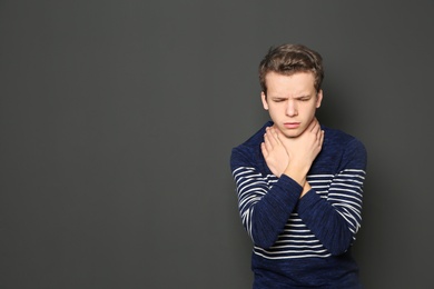 Photo of Teenage boy suffering from cough on dark background. Space for text