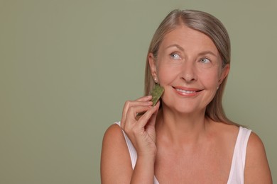 Photo of Woman massaging her face with jade gua sha tool on green background. Space for text