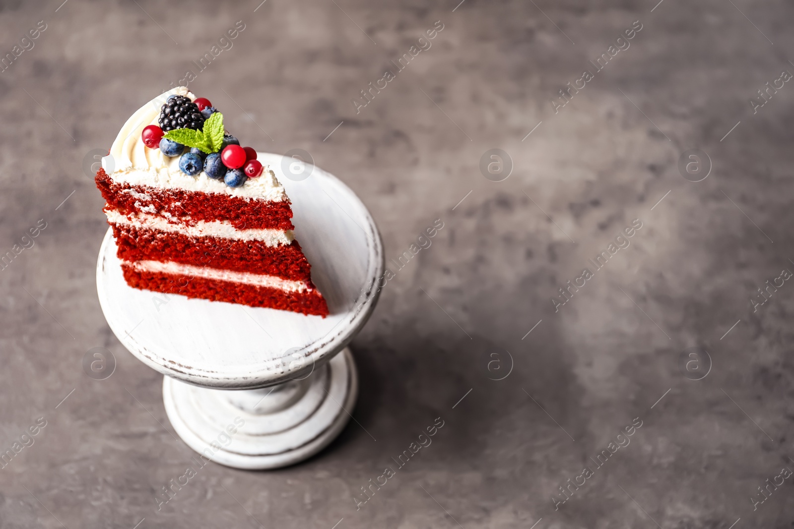 Photo of Stand with piece of delicious homemade red velvet cake and space for text on table