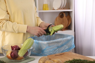 Photo of Woman peeling fresh zucchini above garbage bin indoors, closeup