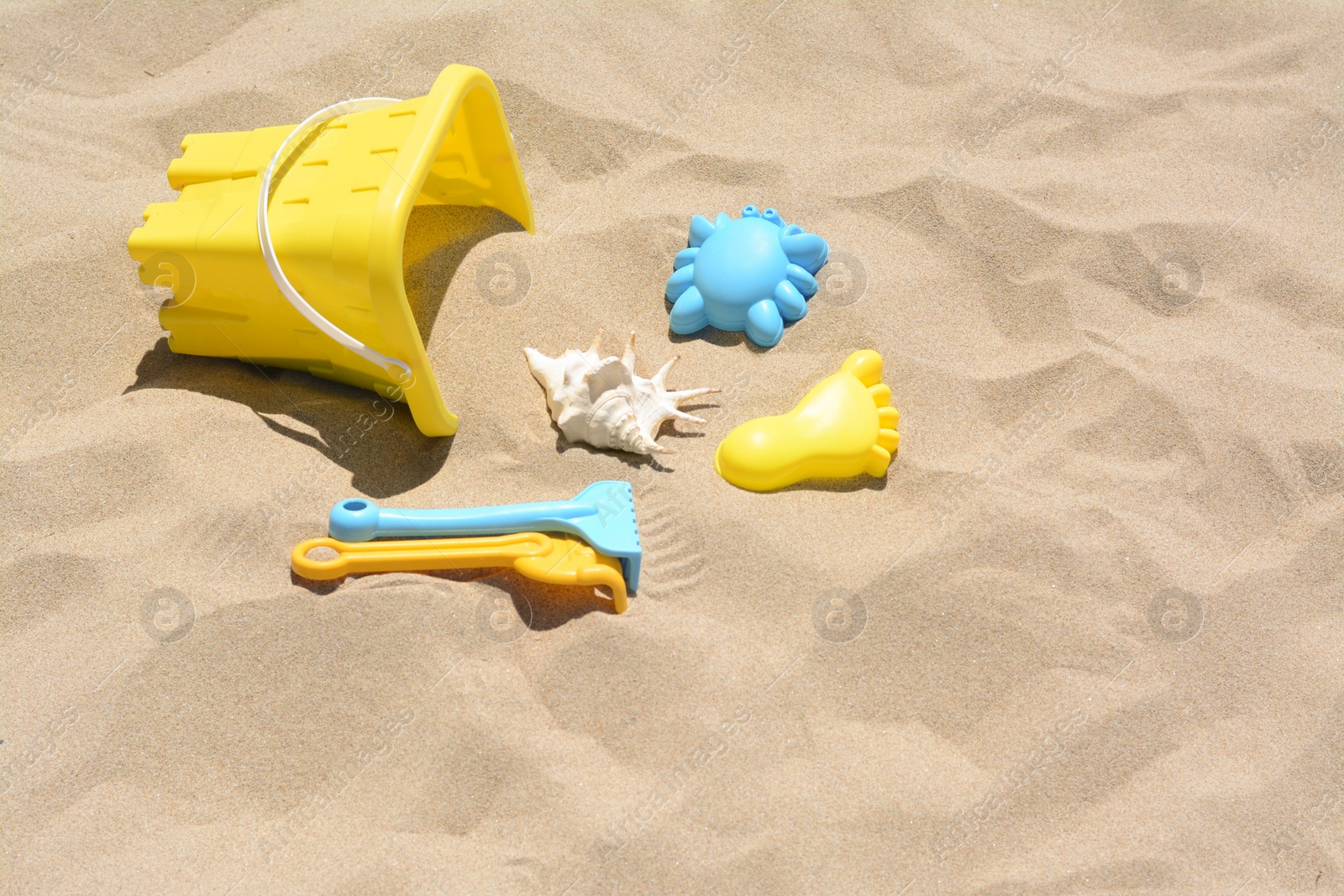 Photo of Bright plastic bucket and rakes on sand. Beach toys. Space for text