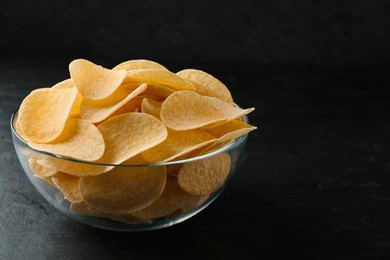 Bowl with delicious potato chips on black table, closeup. Space for text