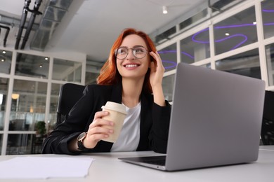 Photo of Happy woman with paper cupcoffee working on laptop at white desk in office