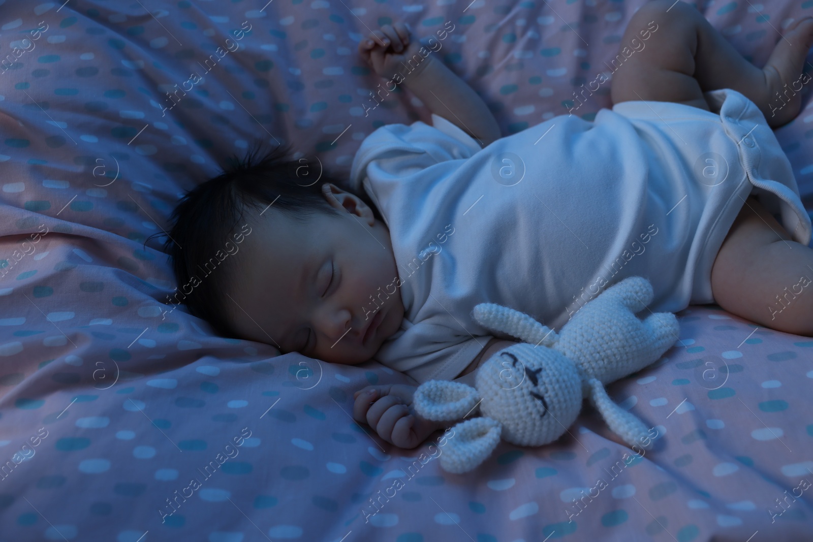Photo of Cute newborn baby sleeping with toy bunny in crib at night