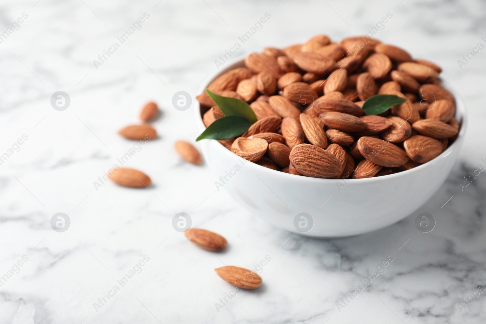 Photo of Tasty organic almond nuts in bowl on table. Space for text