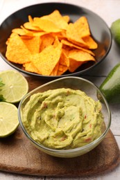 Photo of Bowl of delicious guacamole served with nachos chips and lime on white table