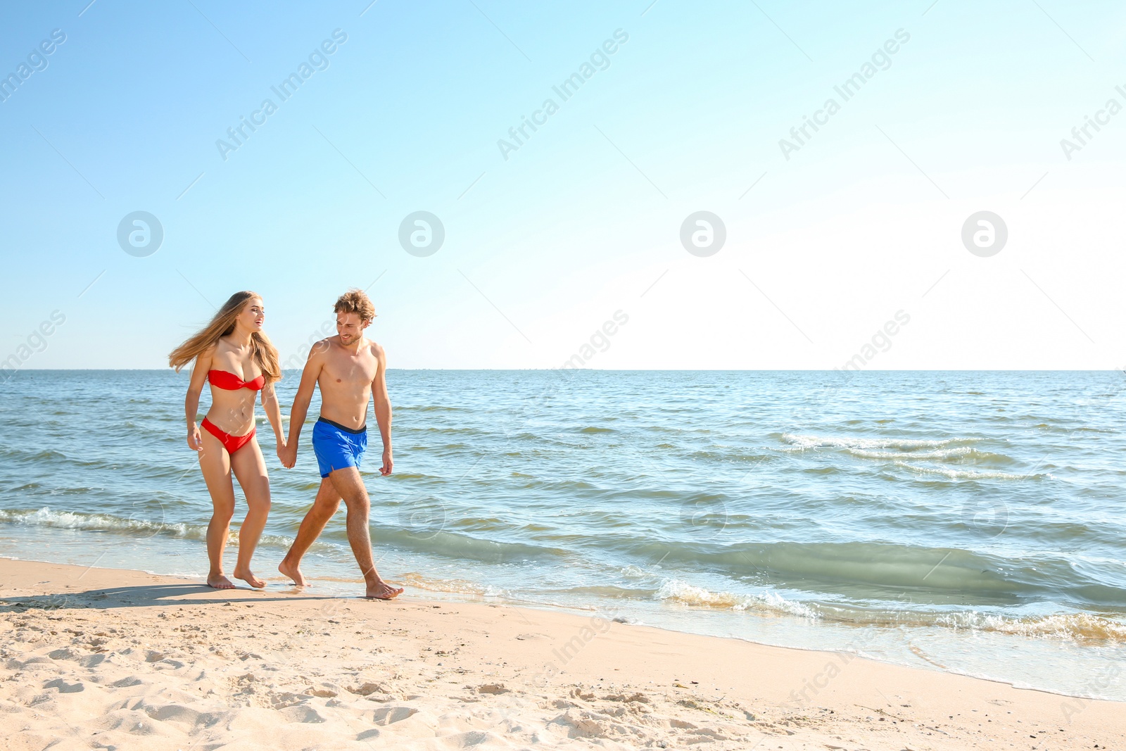 Photo of Happy young couple in beachwear walking together on seashore