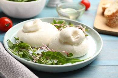 Photo of Delicious burrata cheese with arugula and microgreens served on light blue wooden table, closeup