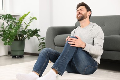Photo of Man suffering from leg pain near sofa in room