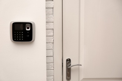 Photo of Modern alarm system with fingerprint scanner near entrance indoors. Space for text