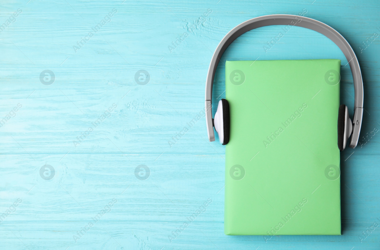 Photo of Book and headphones on light blue wooden background, flat lay. Space for text