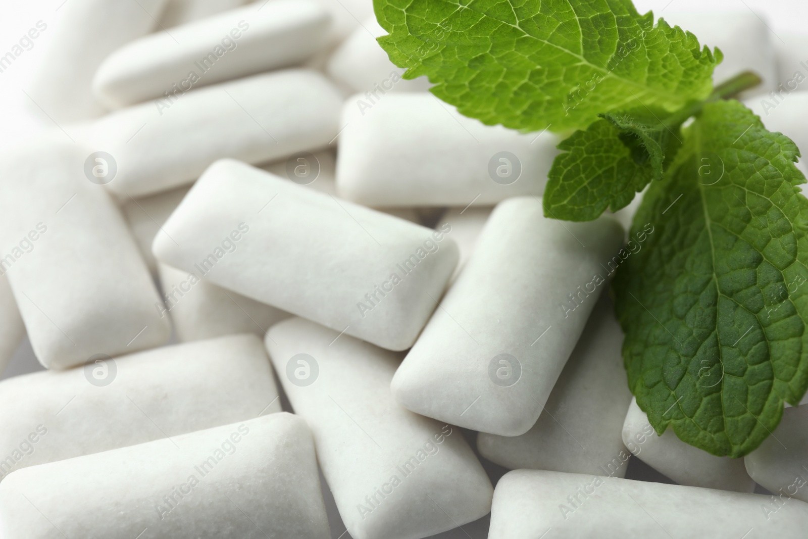 Photo of Tasty white chewing gums and mint leaves as background, closeup