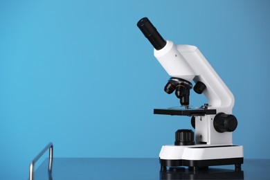 Photo of Modern microscope on metal table against blue background. Space for text