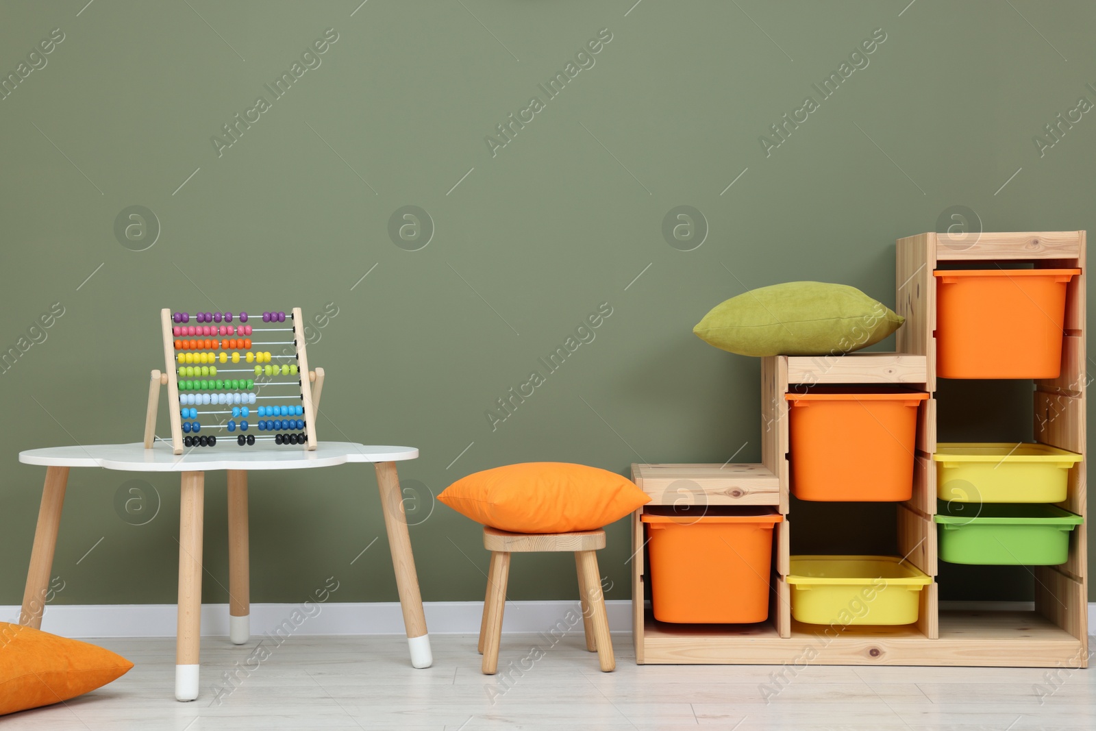 Photo of Table with chair, shelves and abacus toy near olive wall in playroom. Stylish kindergarten interior