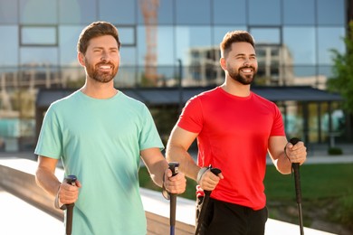 Photo of Happy men practicing Nordic walking with poles outdoors on sunny day