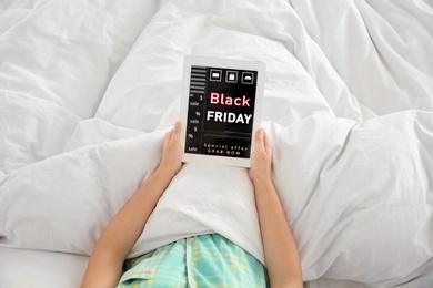 Photo of Woman using tablet with Black Friday announcement while lying in bed, above view