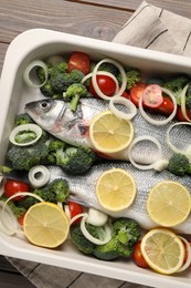 Photo of Raw fish with vegetables and lemon in baking dish on wooden table, top view