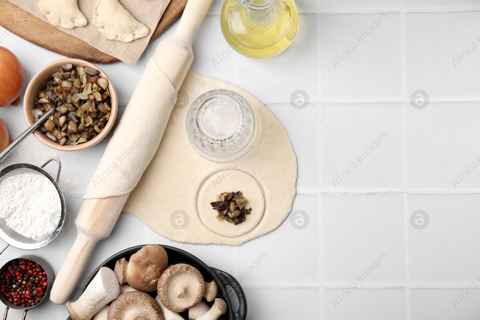 Photo of Process of making dumplings (varenyky) with mushrooms. Raw dough and ingredients on white tiled table, flat lay. Space for text