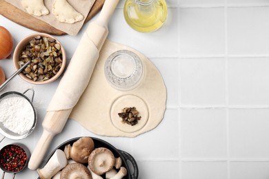 Process of making dumplings (varenyky) with mushrooms. Raw dough and ingredients on white tiled table, flat lay. Space for text