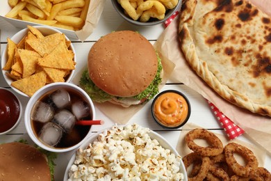 Photo of Burgers, chips and other fast food on white wooden table, flat lay