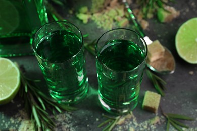 Absinthe in shot glasses, brown sugar, lime and rosemary on gray table, closeup. Alcoholic drink