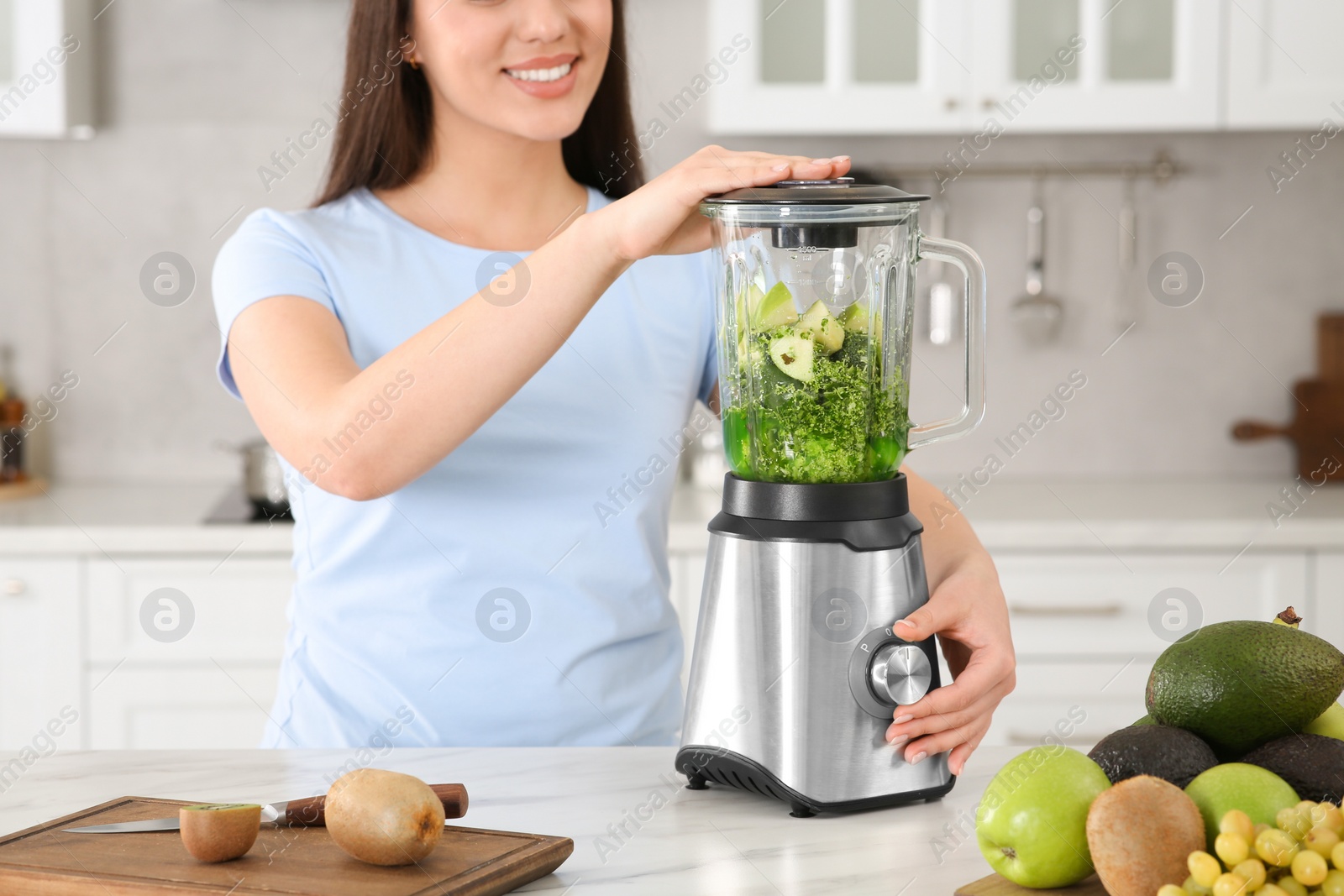 Photo of Woman preparing tasty smoothie at white table in kitchen, closeup