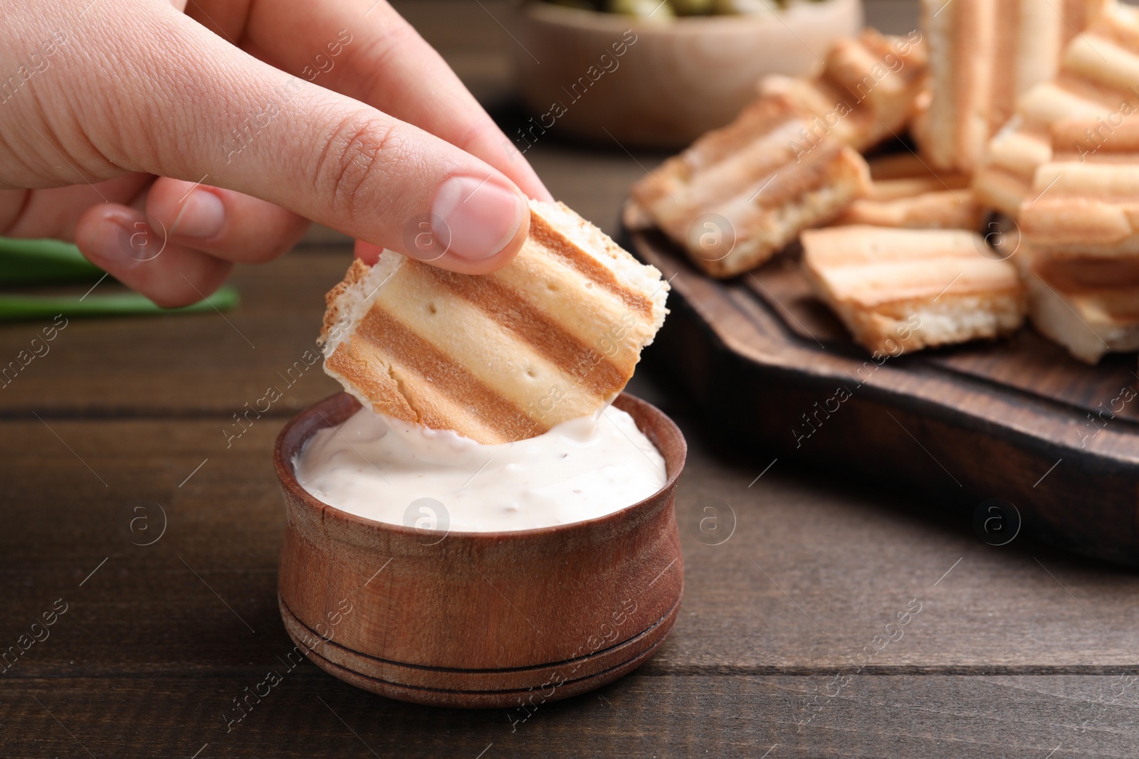 Photo of Woman dipping pita chip into sauce at wooden table, closeup