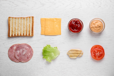 Fresh ingredients for tasty sandwich on white wooden background, flat lay