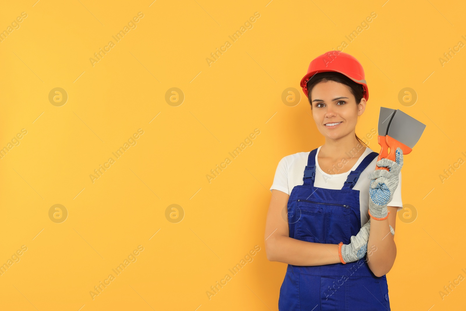 Photo of Professional worker with putty knives in hard hat on orange background, space for text