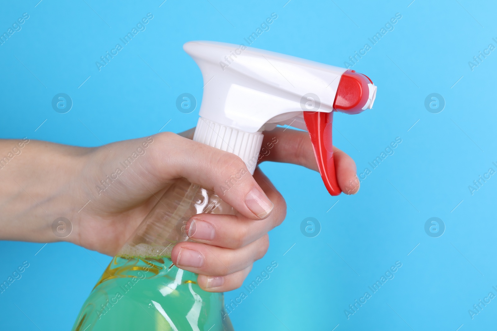 Photo of Woman holding plastic spray bottle on light blue background, closeup