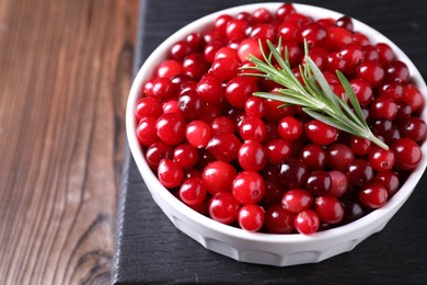 Photo of Fresh ripe cranberries and rosemary in bowl on wooden table, closeup