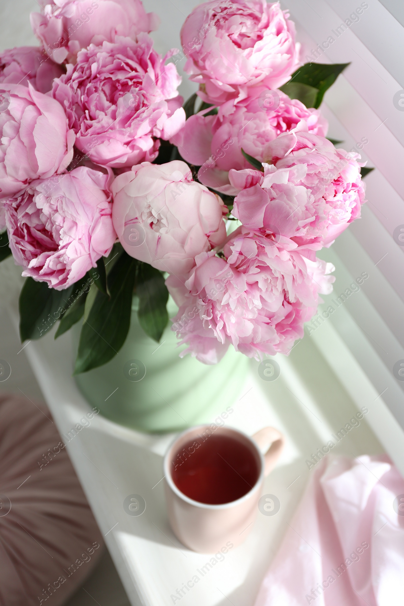 Photo of Bouquet of beautiful peonies and cup of tea on window sill