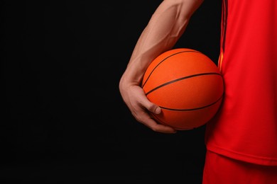 Athletic man with basketball ball on black background, closeup. Space for text