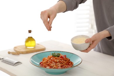 Photo of Food stylist adding grated cheese to spaghetti at white wooden table in photo studio, closeup