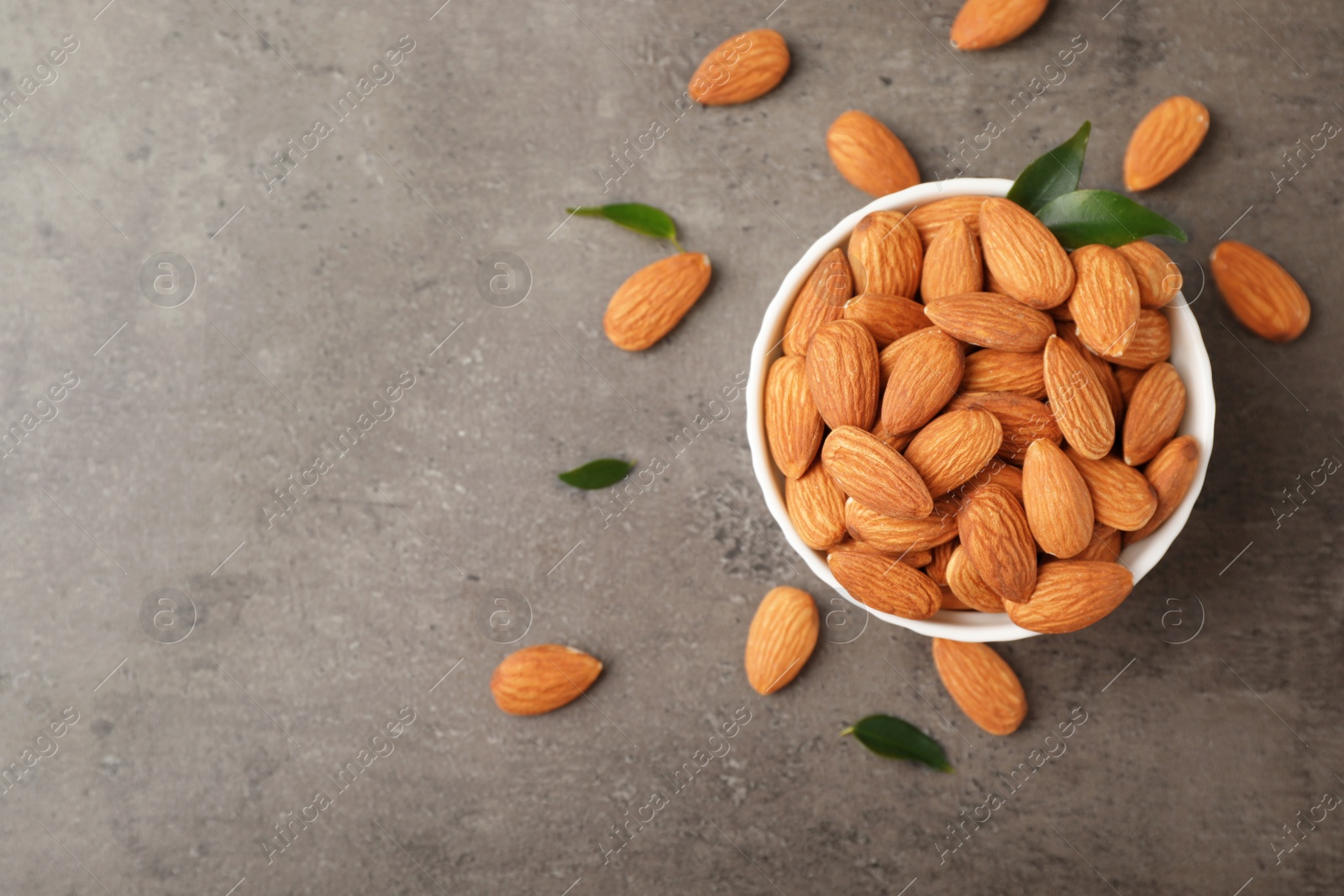 Photo of Tasty organic almond nuts in bowl and space for text on table, top view