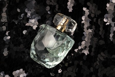 Photo of Luxury perfume in bottle on fabric with shiny sequins, above view