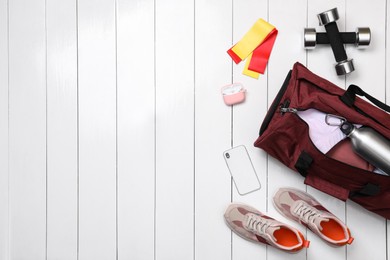 Photo of Gym bag and sports equipment on white wooden background, flat lay. Space for text