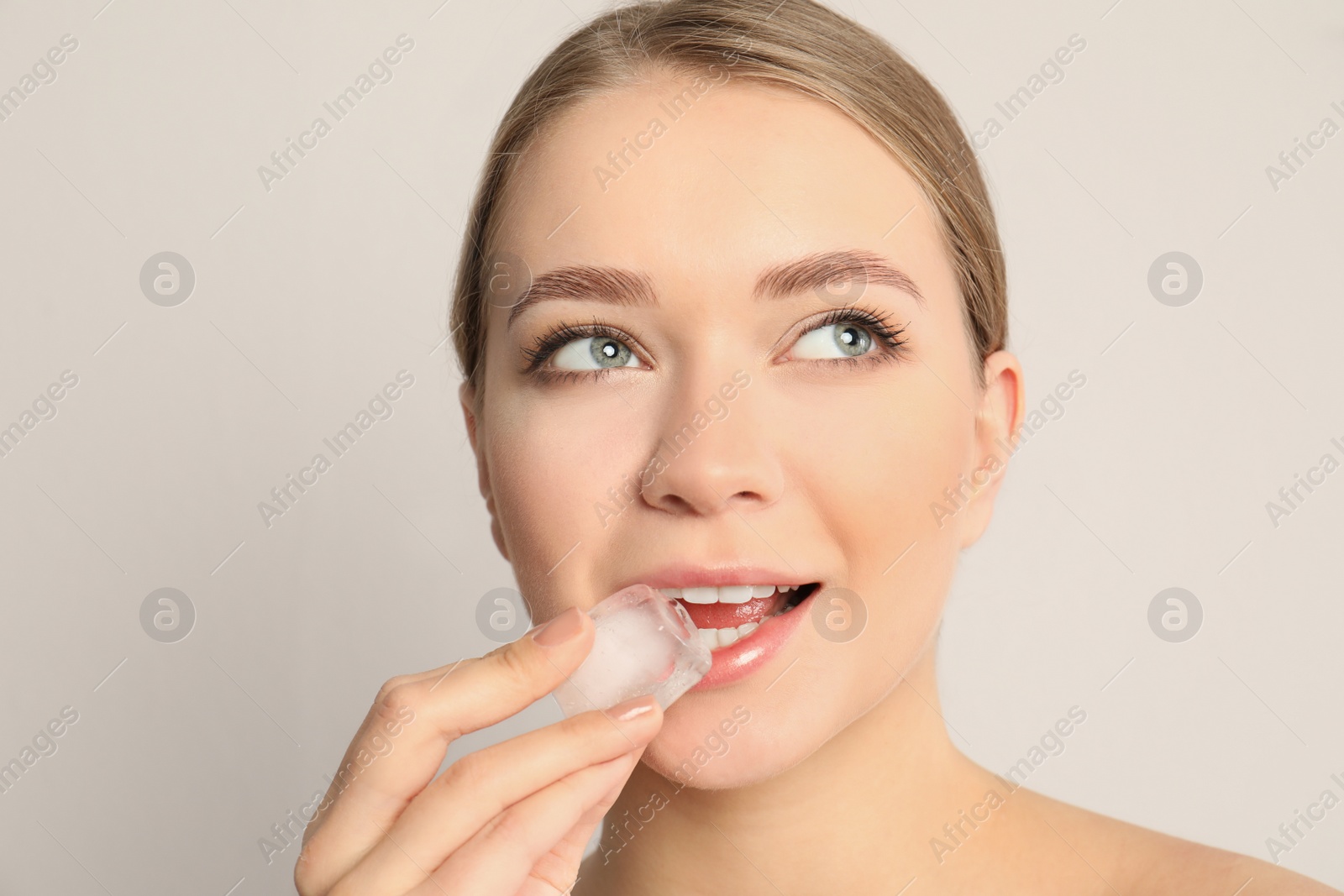 Photo of Young woman with ice cube on light background