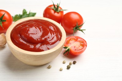 Photo of Delicious ketchup in bowl, peppercorns and tomatoes on white wooden table, closeup. Space for text