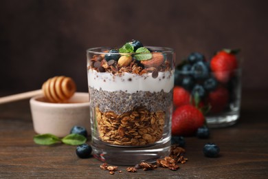 Photo of Tasty granola with berries, nuts, yogurt and chia seeds in glass on wooden table