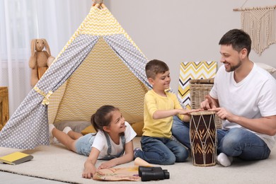 Photo of Father and children playing near toy wigwam at home