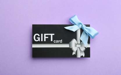 Photo of Gift card with bow on violet background, top view