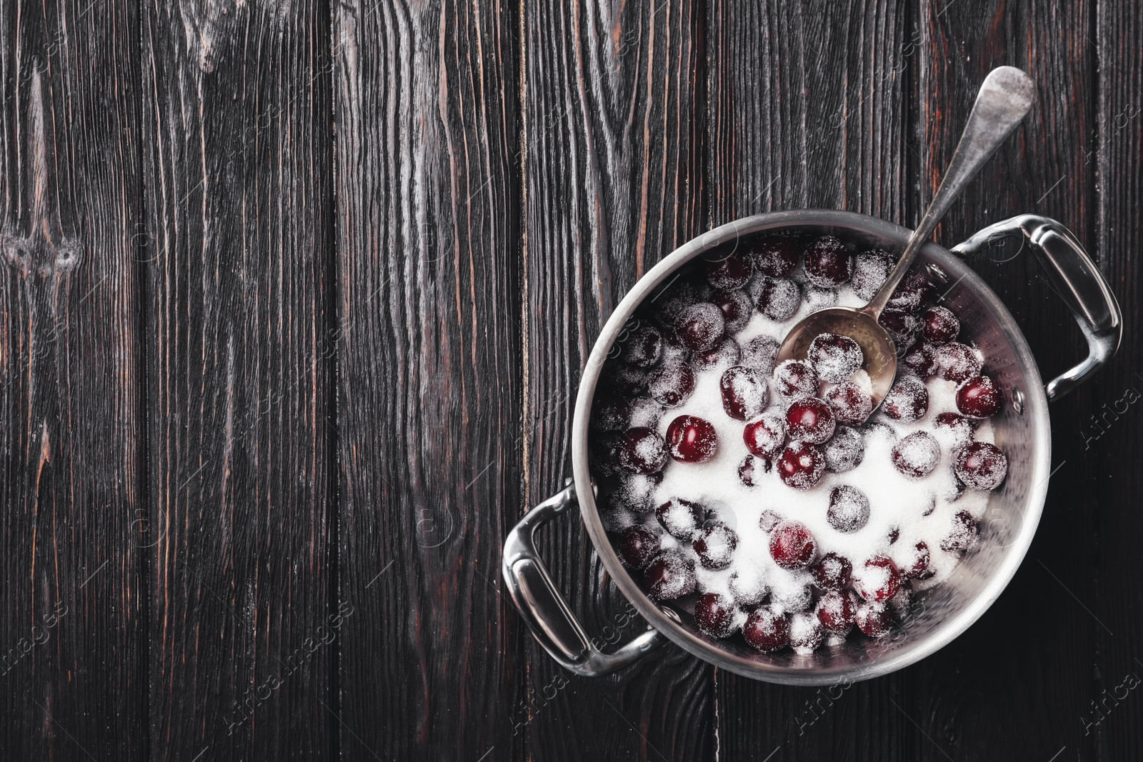 Photo of Pot with cherries and sugar on black wooden table, top view. Making of delicious jam