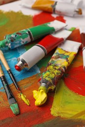 Photo of Tubes of colorful oil paints and brushes on canvas with abstract painting