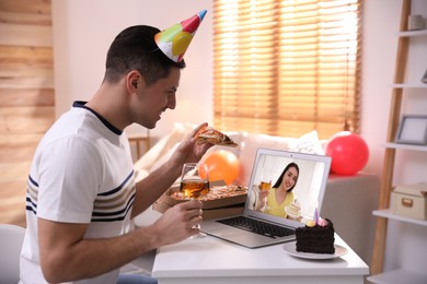 Man with glass of wine, pizza and cake having online party via laptop at home during quarantine lockdown