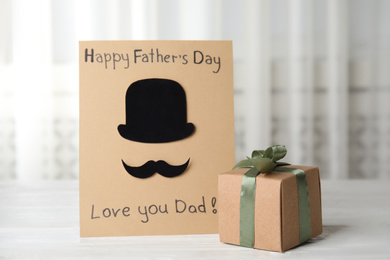 Photo of Greeting card with phrase HAPPY FATHER'S DAY I LOVE YOU DAD and gift box on white wooden table indoors