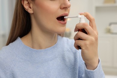 Photo of Adult woman using throat spray at home, closeup