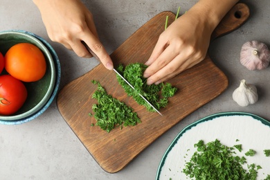 Woman cutting fresh green parsley on wooden board, top view