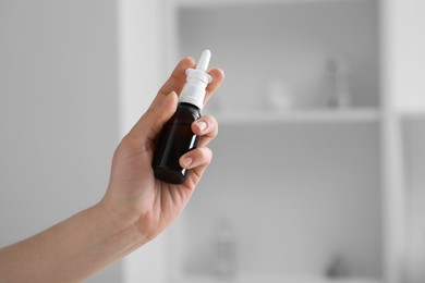 Woman holding nasal spray bottle indoors, closeup. Space for text